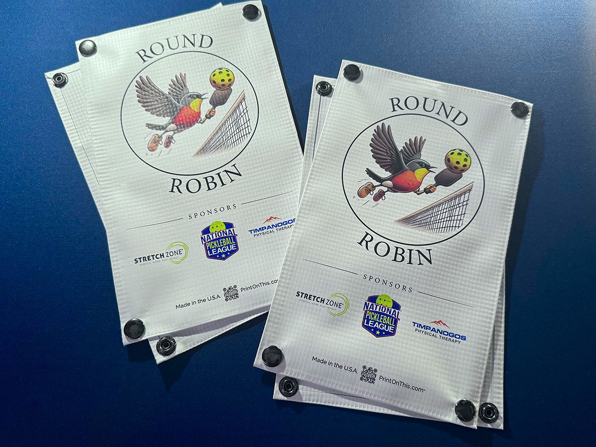 Round Robin pickleball tournament net signs showing sponsor logos and court branding on the same net